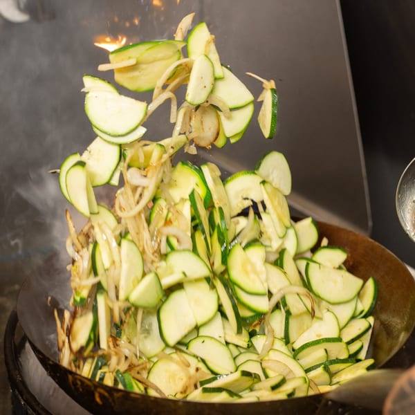 Zucchini and onions stir-frying in a wok with flames and smoke at Oryza Asian Grill.