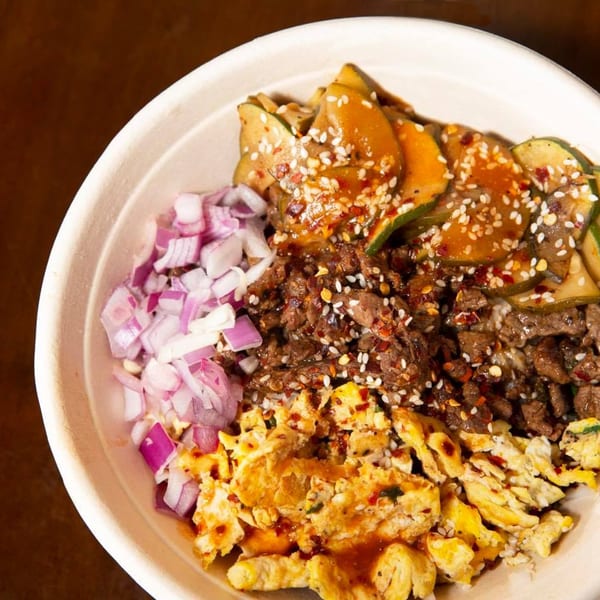 Close-up of an Oryza Asian Grill bowl with beef, scrambled egg, red onion, and zucchini.