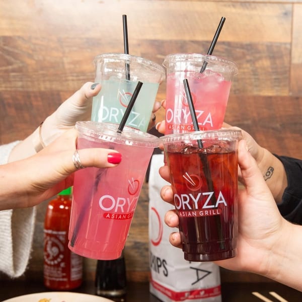 Four hands holding up Oryza Asian Grill drinks in clear cups, toasting together.