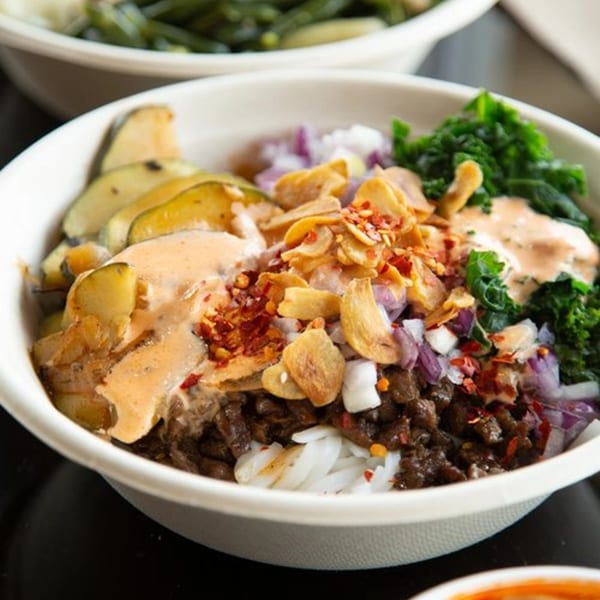 Oryza Asian Grill bowl with rice, meat, vegetables, sauce, and crispy garlic.