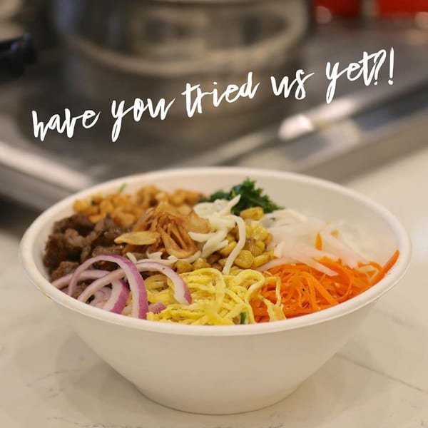 A colorful Oryza Asian Grill bowl with beef, corn, onions, carrots, and egg strips.