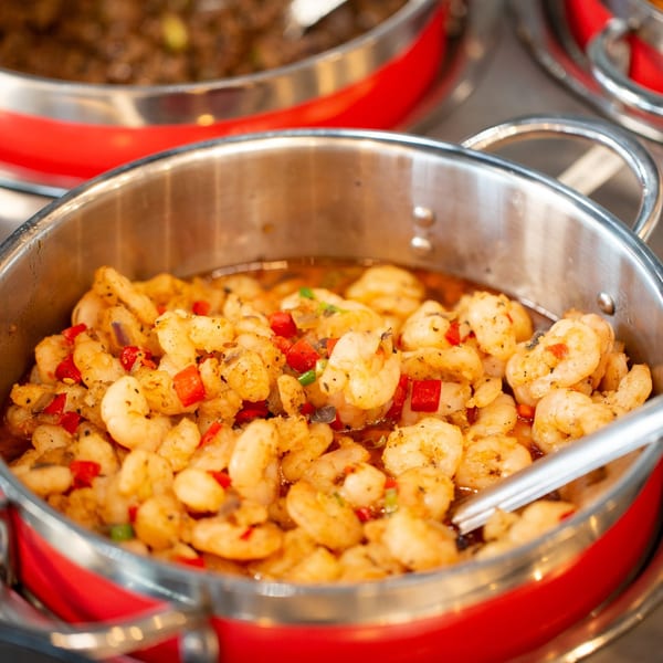 Close-up of a stainless steel pan filled with seasoned shrimp and red bell peppers at Oryza Asian Grill.